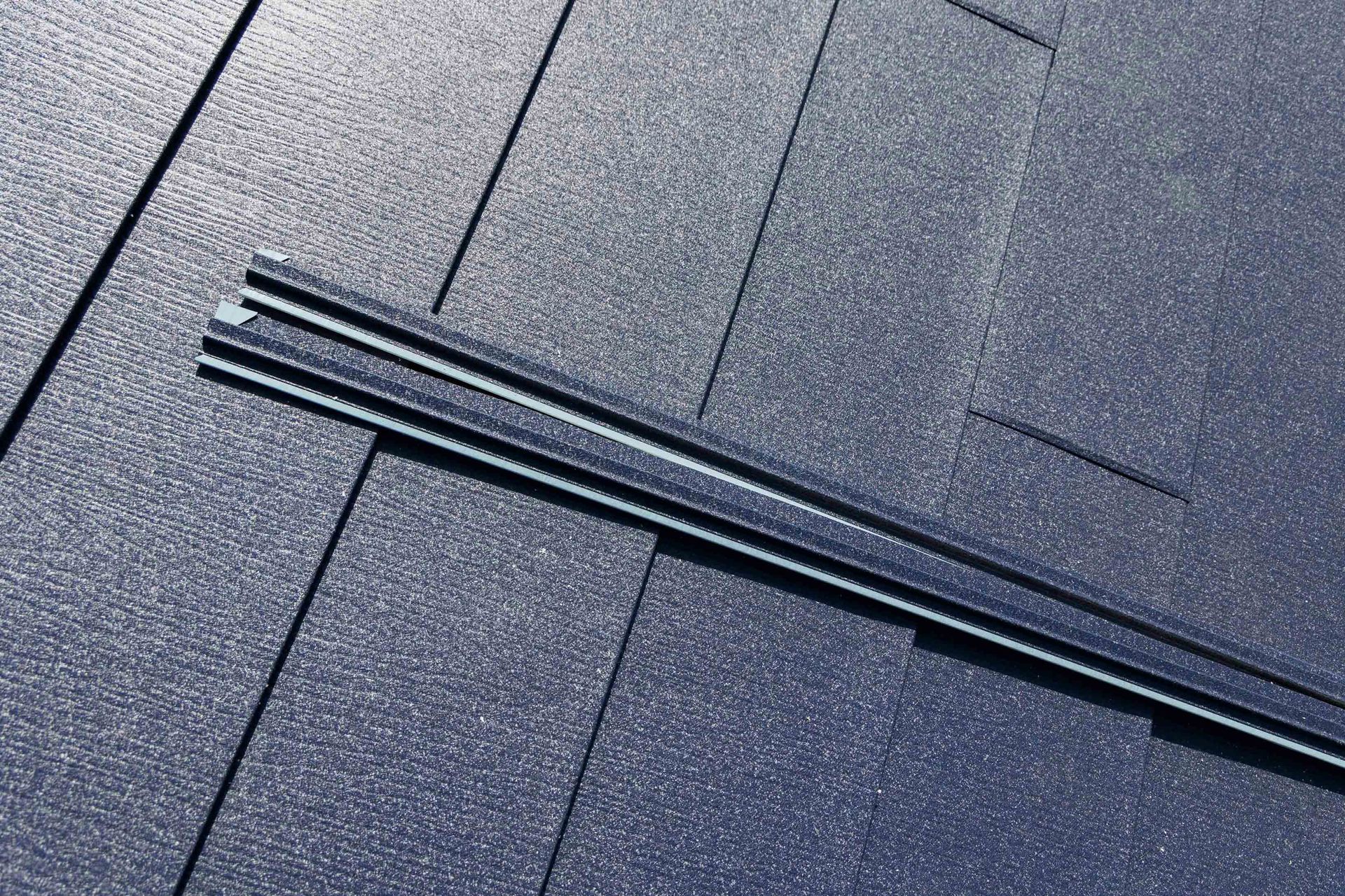 Close-up of dark gray roof shingles with a long metal roof vent running diagonally across them