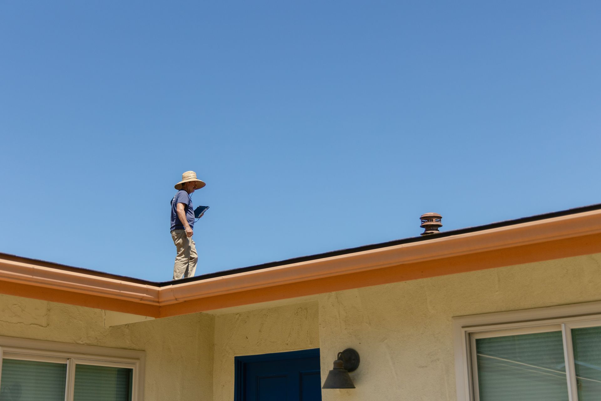 Worker on a roof edge under a clear blue sky, near the house gutter and eaves.