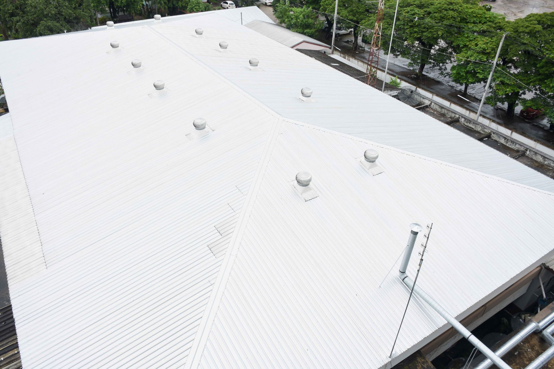 White metal roof with several vents, seen from above near trees and scaffolding