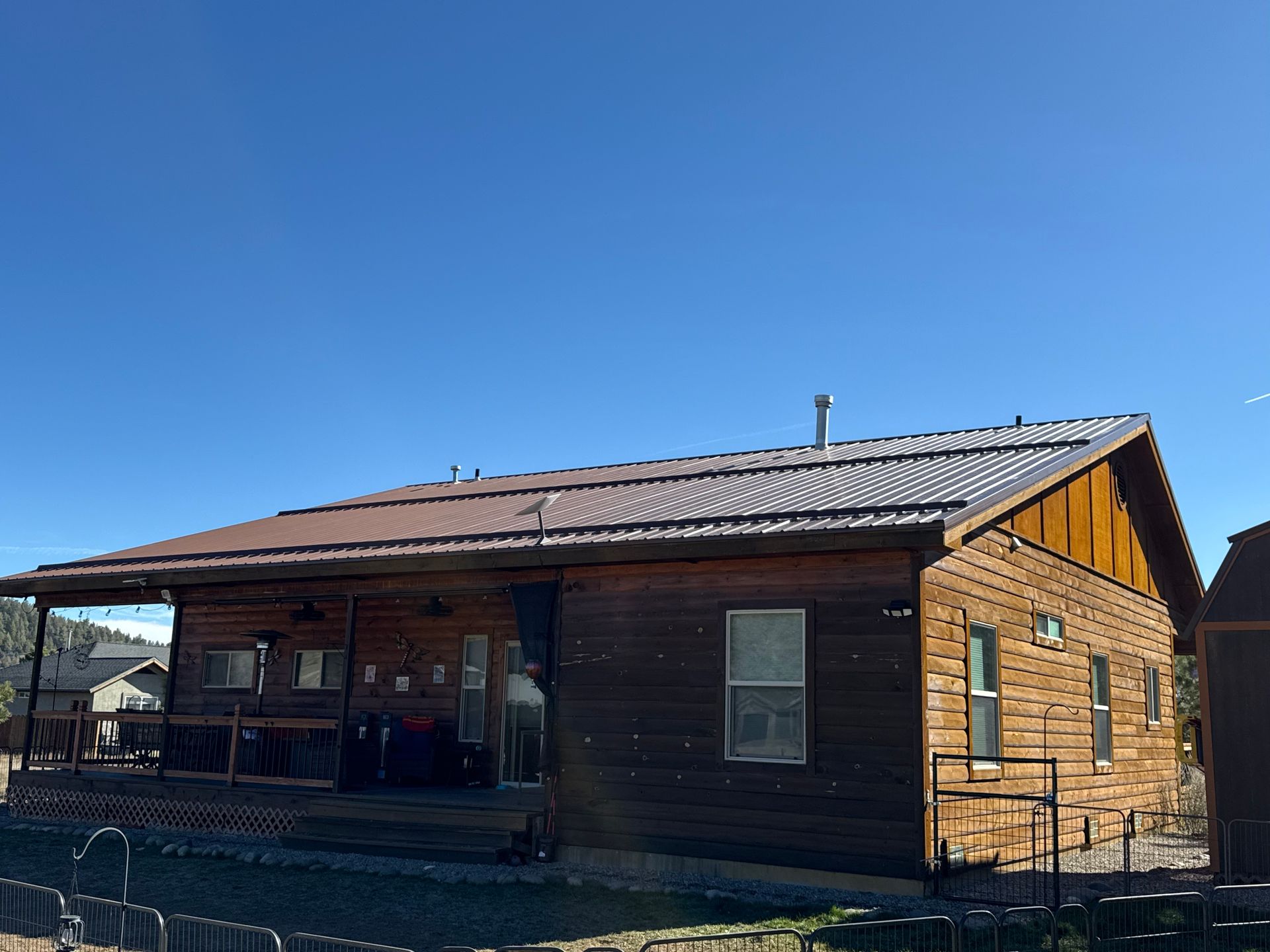 Wooden cabin with a brown roof under a clear blue sky, viewed from the front corner.