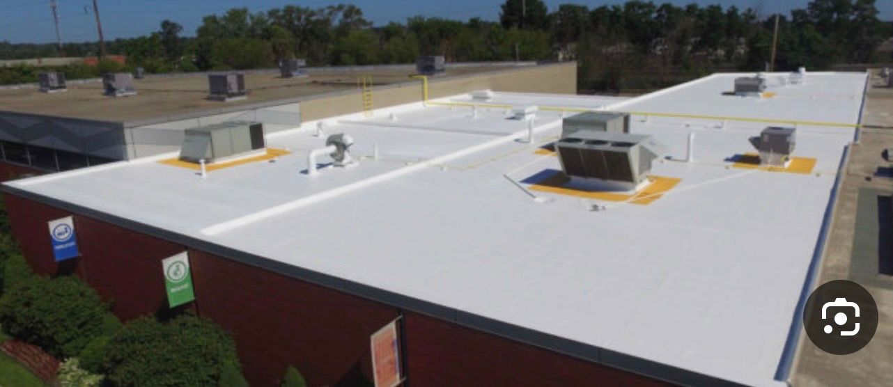 Aerial view of a white flat-roof building with rooftop HVAC units and surrounding greenery