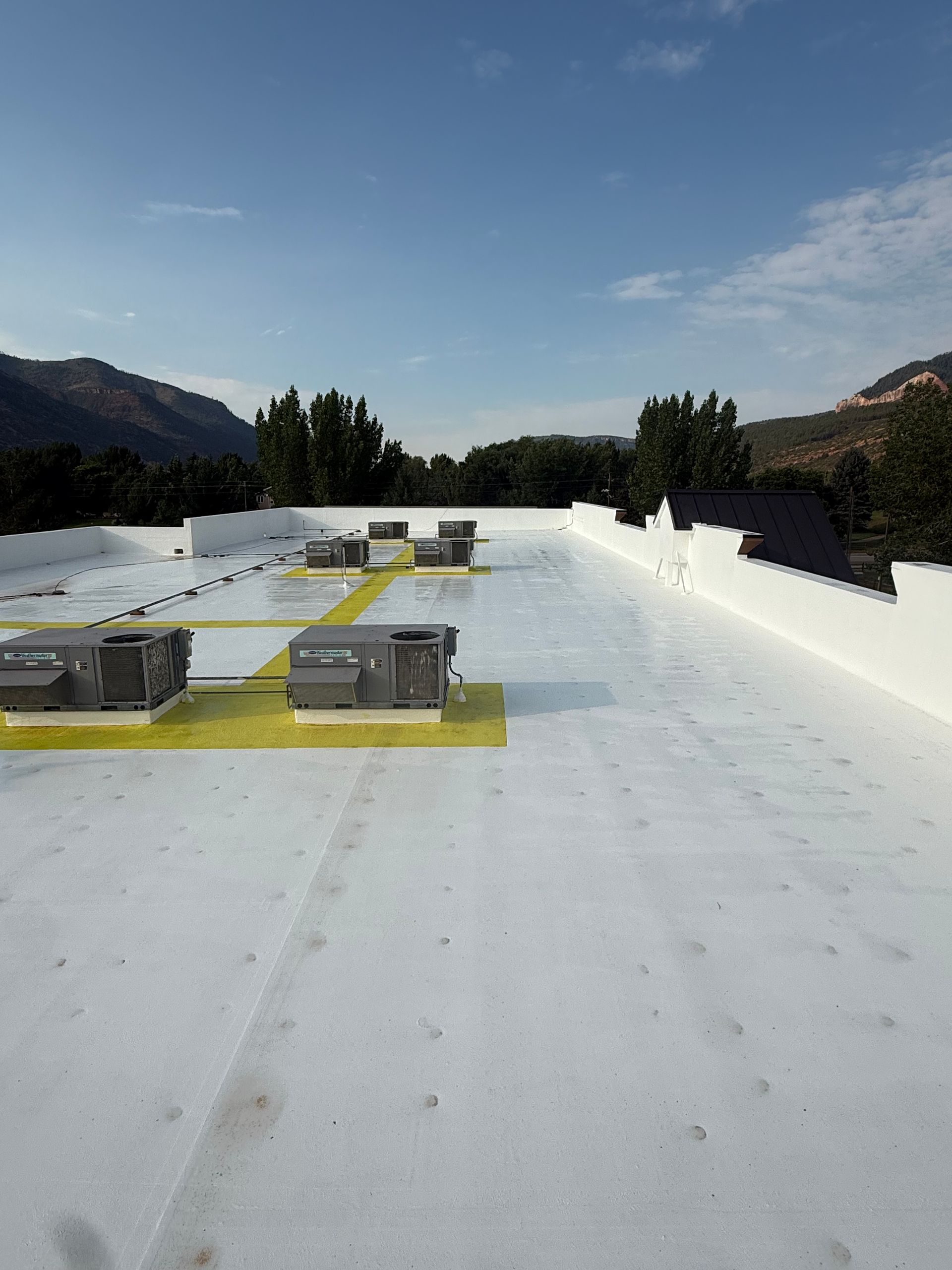 Rooftop with white reflective surface, vents, and distant mountains under a clear blue sky