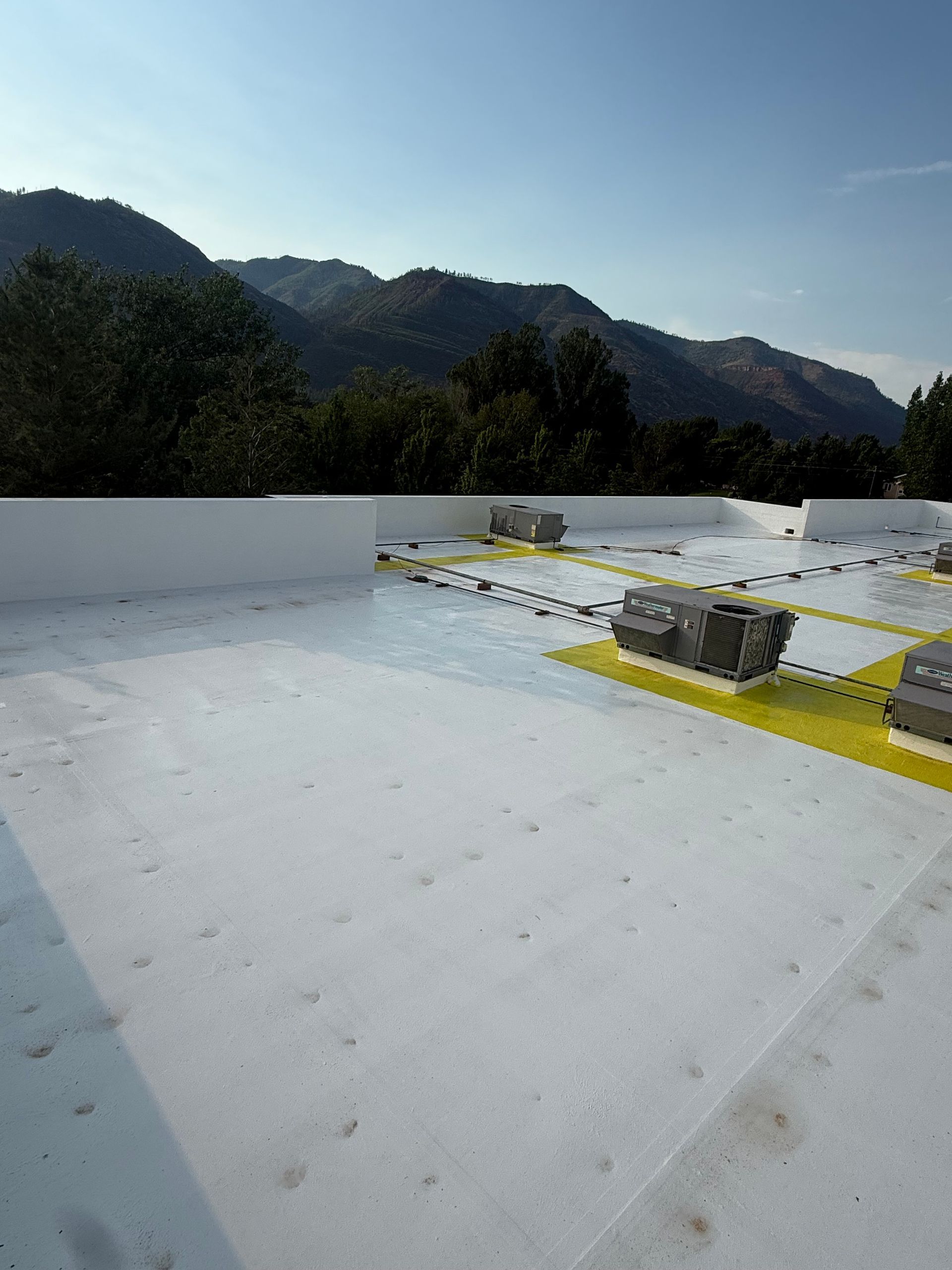White rooftop with yellow safety markings, set against mountain ridges and a clear blue sky.