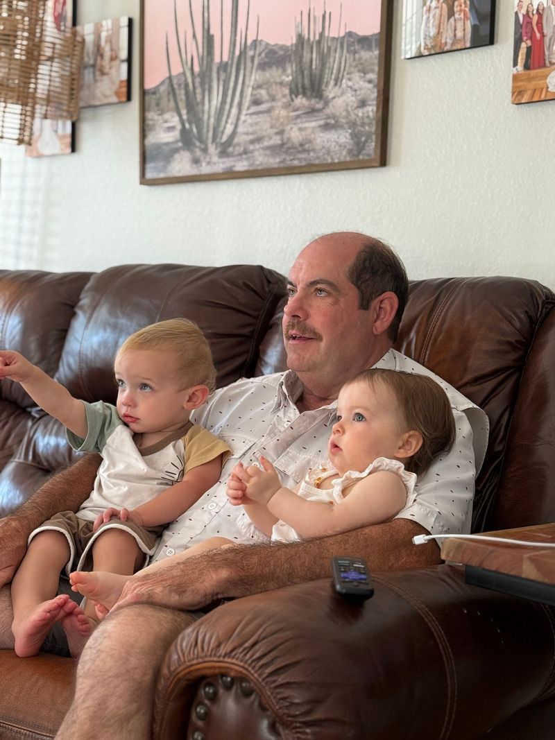 Man sitting on a brown couch holding two small children in a cozy living room