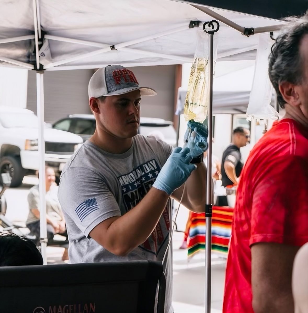Volunteer at an outdoor market wearing gloves, holding a hanging item under a white canopy.