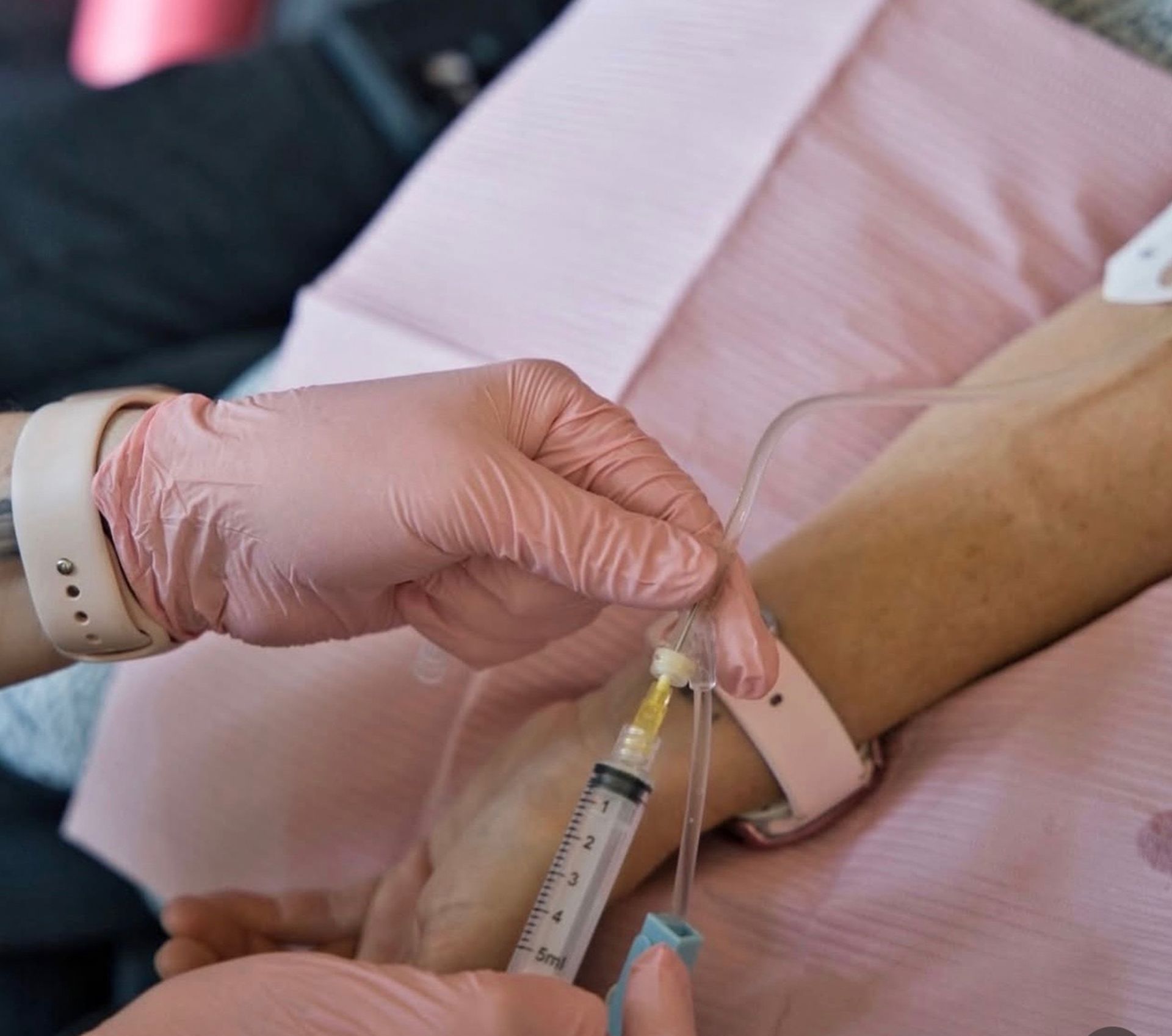 Gloved hands drawing blood from a patient’s arm with a syringe in a clinical setting