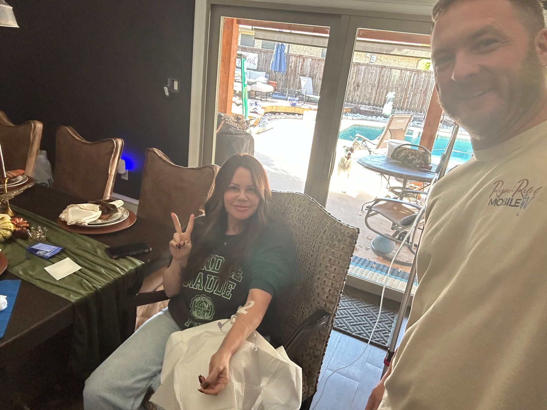 Two people smiling at a restaurant table, one holding up a peace sign, with bright outdoor seating behind them