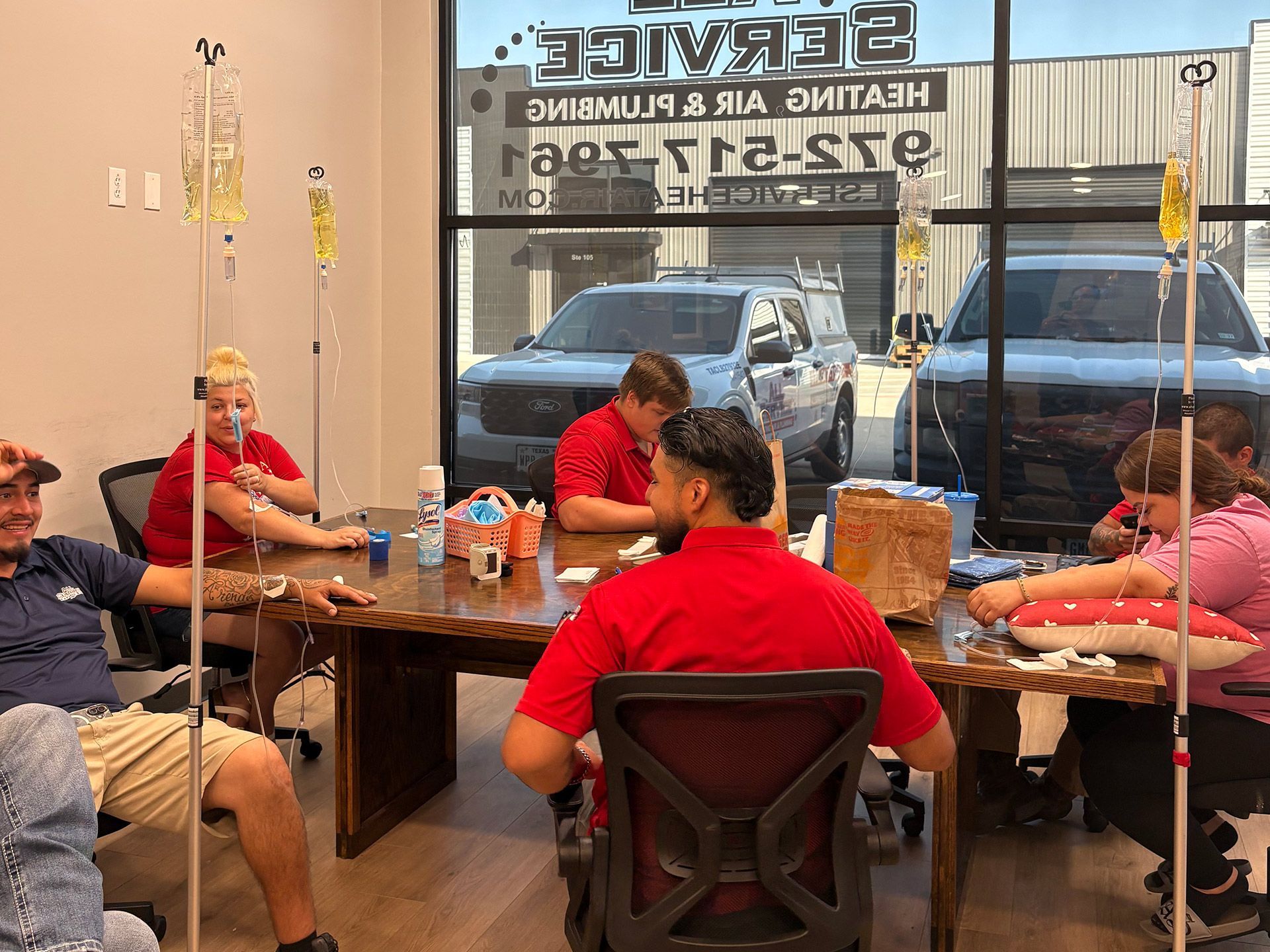 People seated around a wooden table in a bright storefront, chatting and eating near the window.