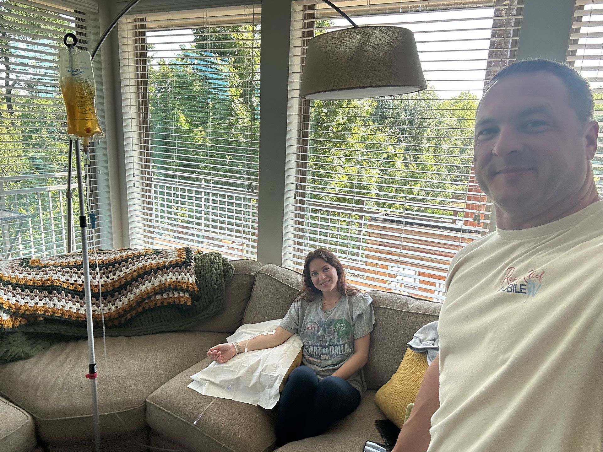 Woman on a beige couch in a bright sunroom, with a man smiling in the foreground.