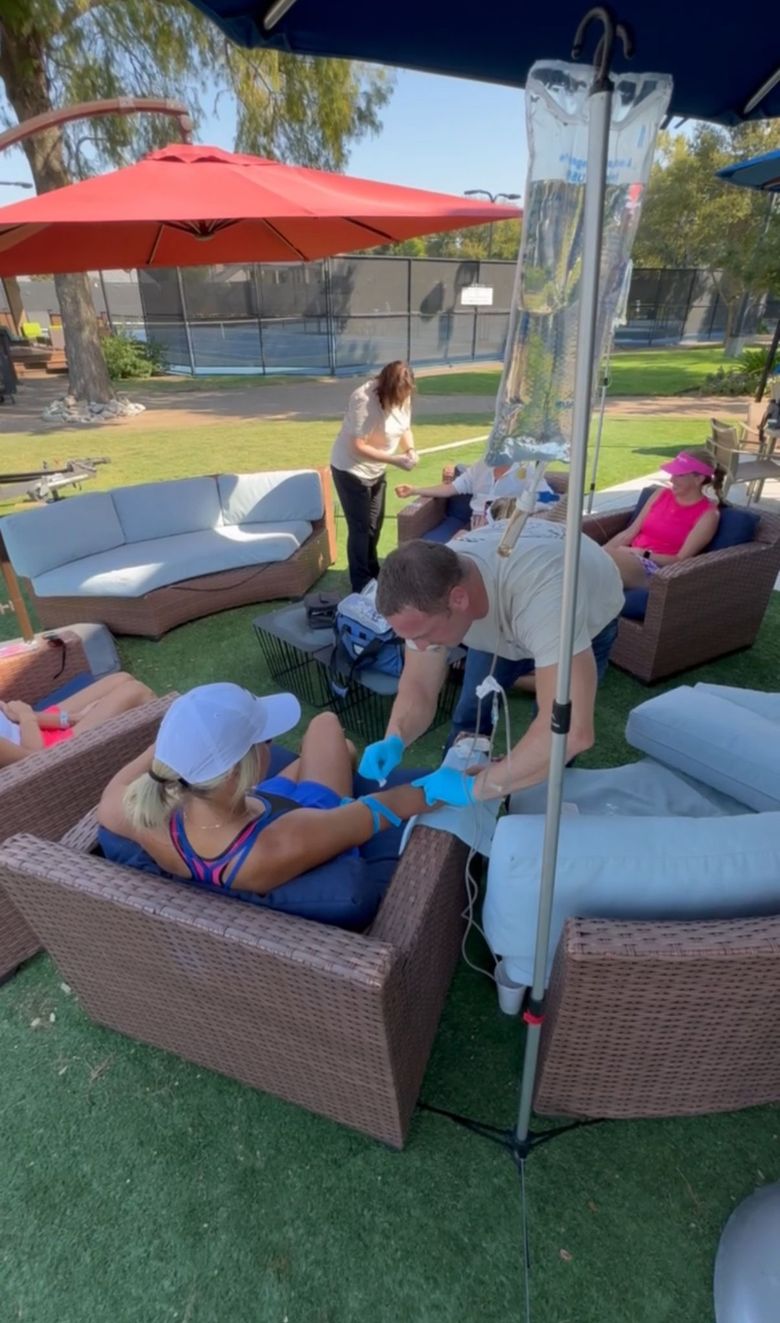 People relaxing outdoors around a patio fire pit under a red umbrella, with cushioned chairs and a heater