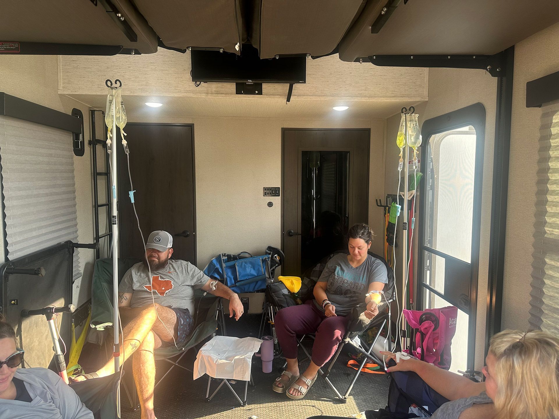 People relaxing in chairs inside a screened-in patio with a TV and sunlight streaming in