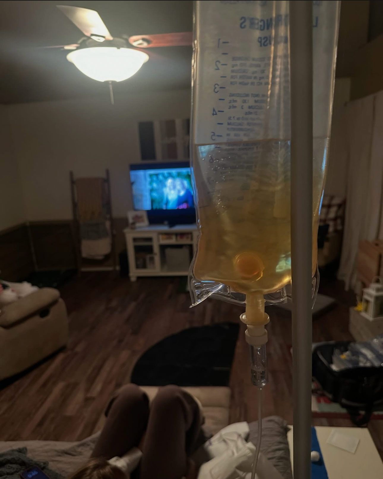 IV drip bag hanging in a living room, with a TV and couch in the background.
