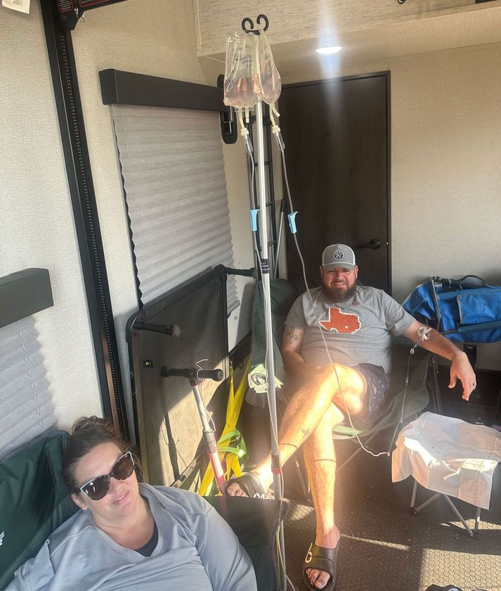 Two people relaxing on a porch with a hanging chair, cooler, and blue bag nearby.