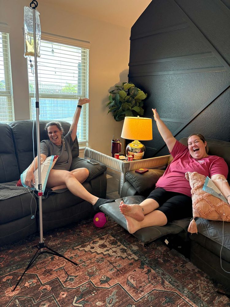 Two people relaxing on couches, smiling and raising their arms in a cozy living room.
