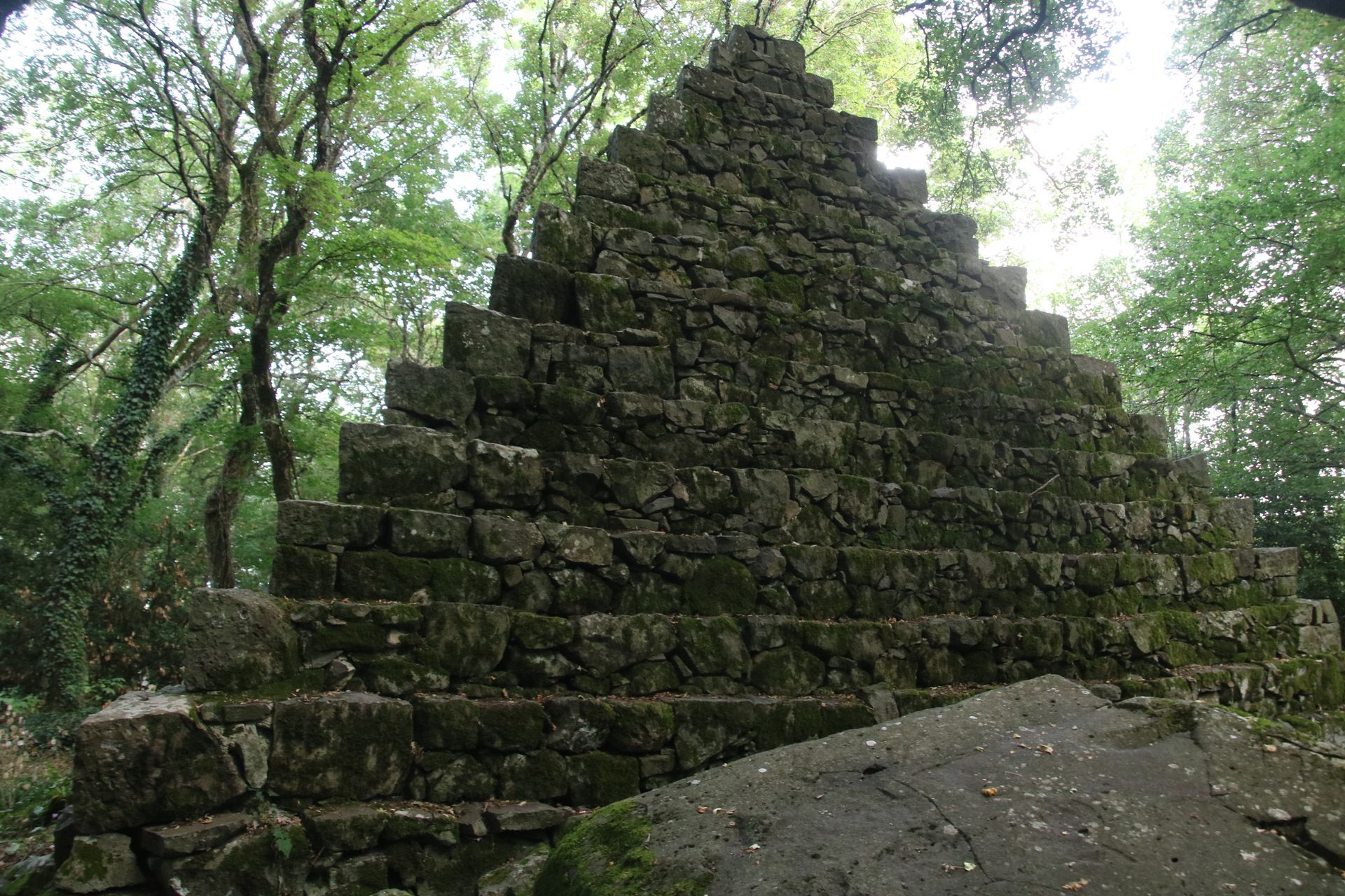A large stone pyramid in the middle of a forest.