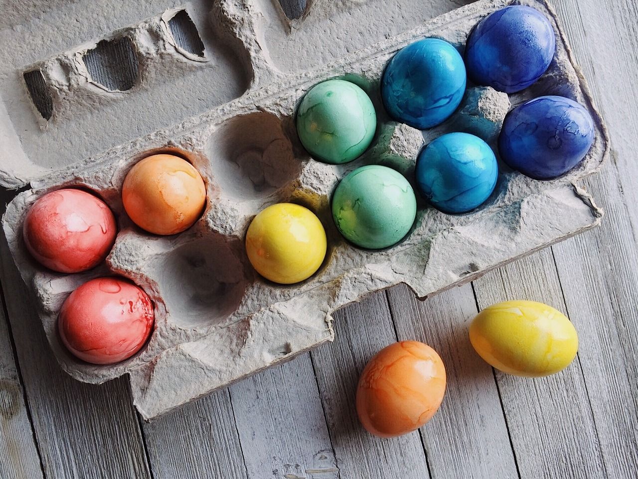 A carton of colorful easter eggs on a wooden table.