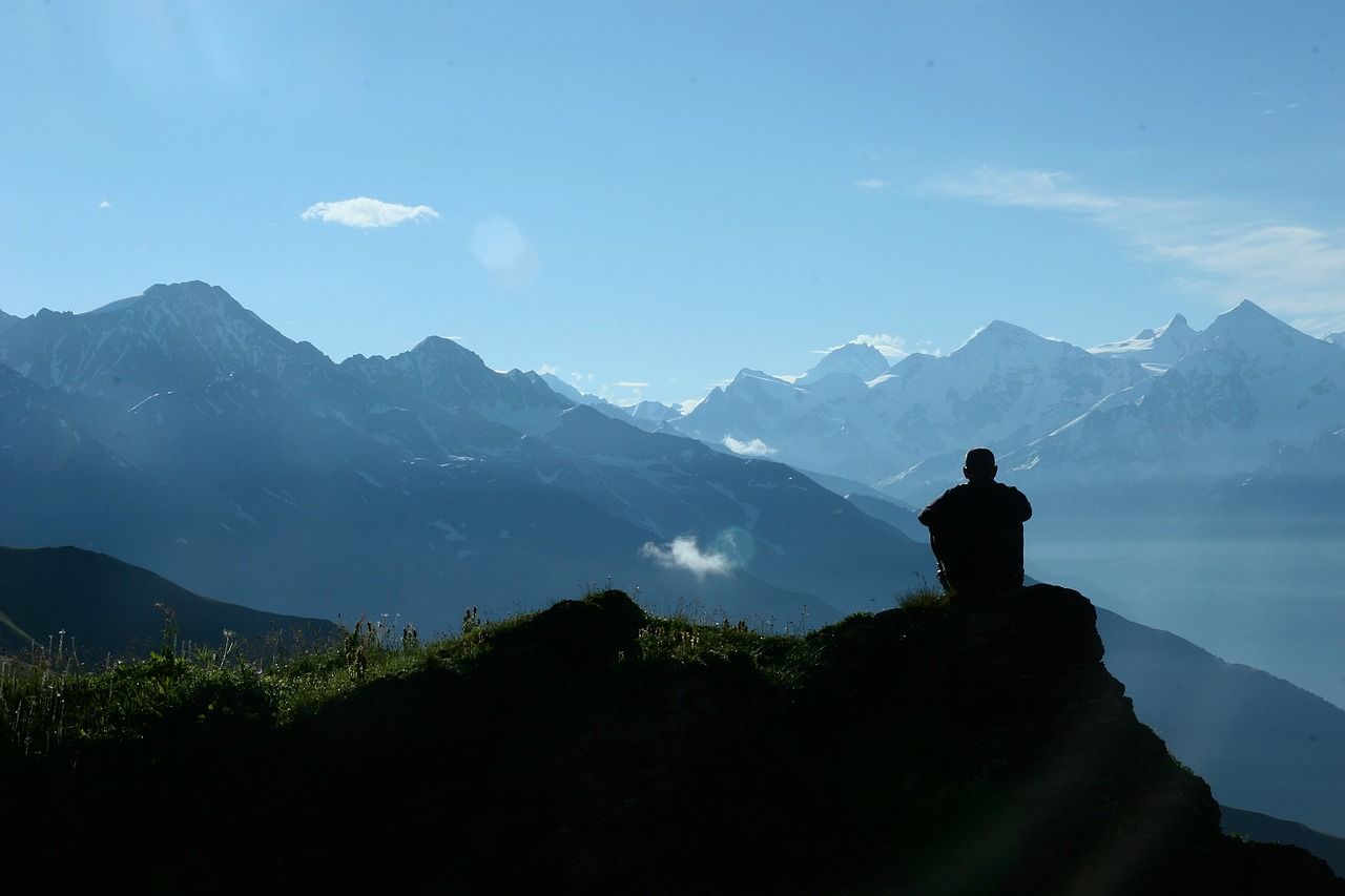 A person is sitting on top of a mountain looking at the mountains.