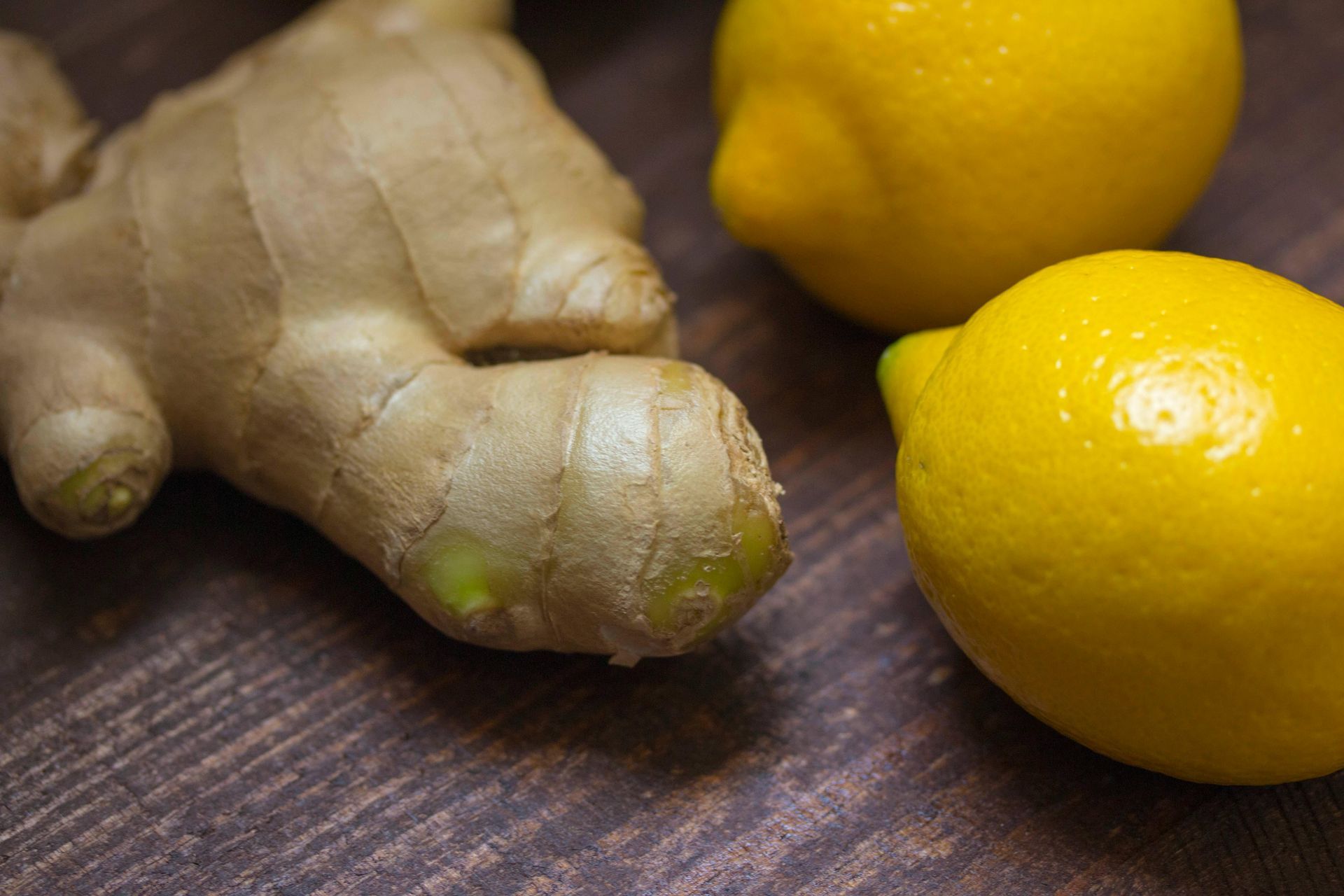 A close up of ginger and lemons on a wooden table.