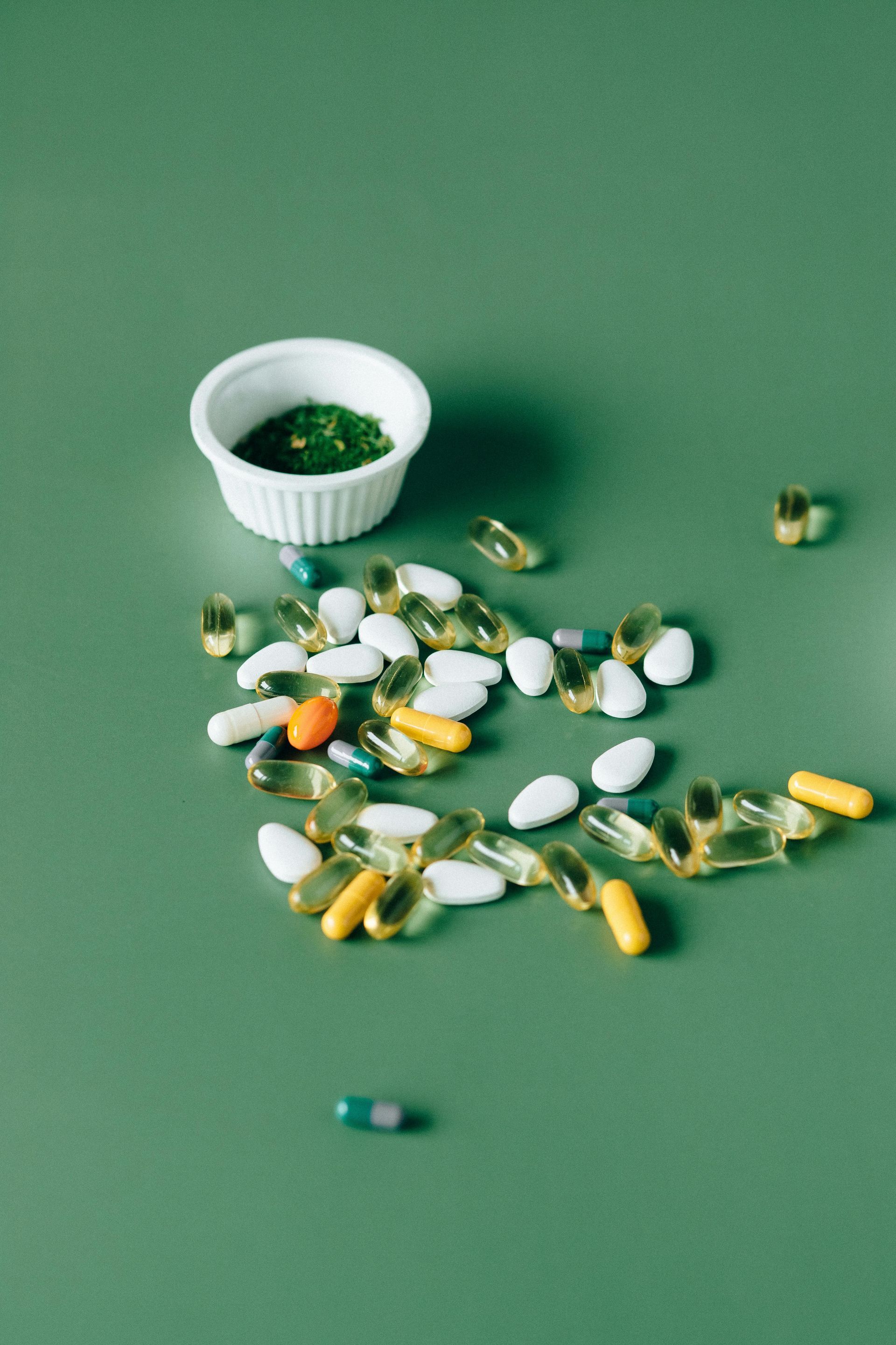 A bowl of green sauce and a pile of pills on a green table.