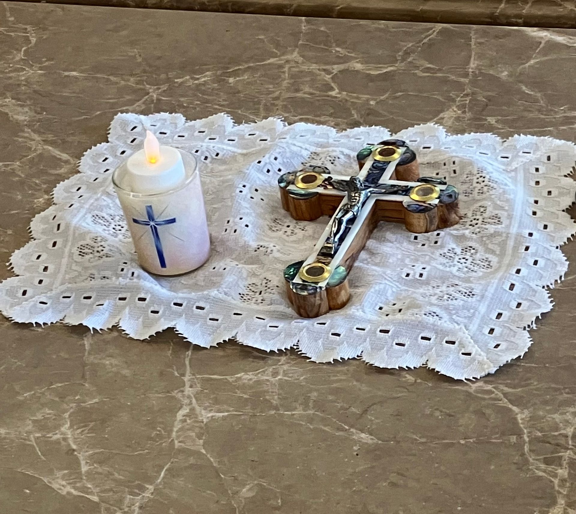 White candle and ornate cross on a lace doily on a marble table