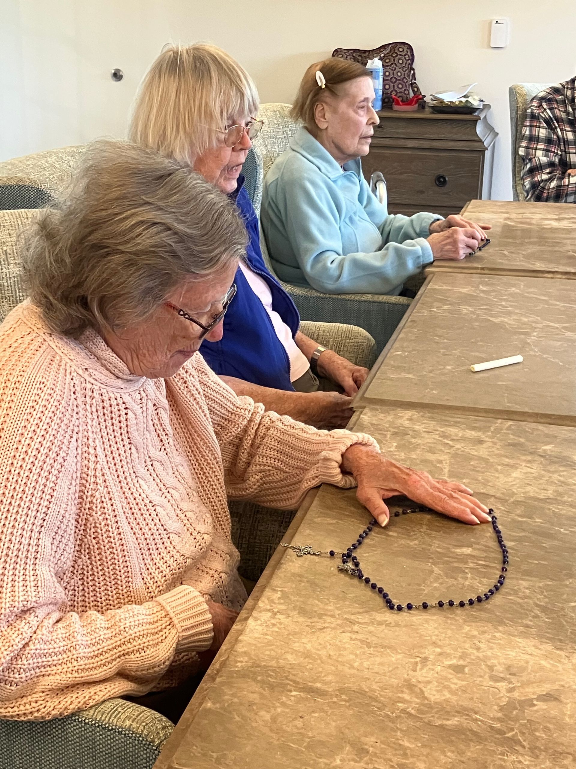 Three people seated at a table, with a beaded necklace laid out in front of them.