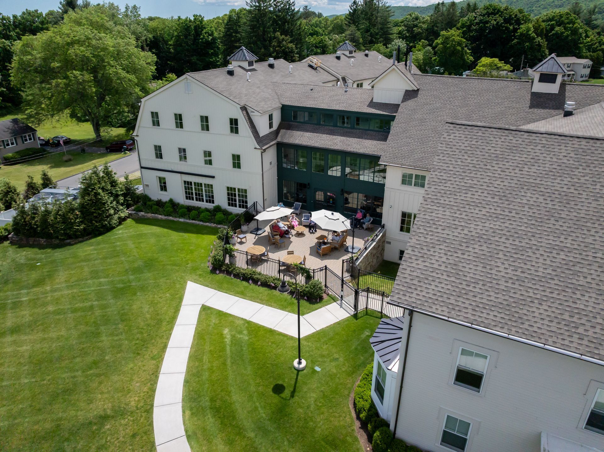 Aerial view of a white hotel with a patio, umbrellas, and a large green lawn in front