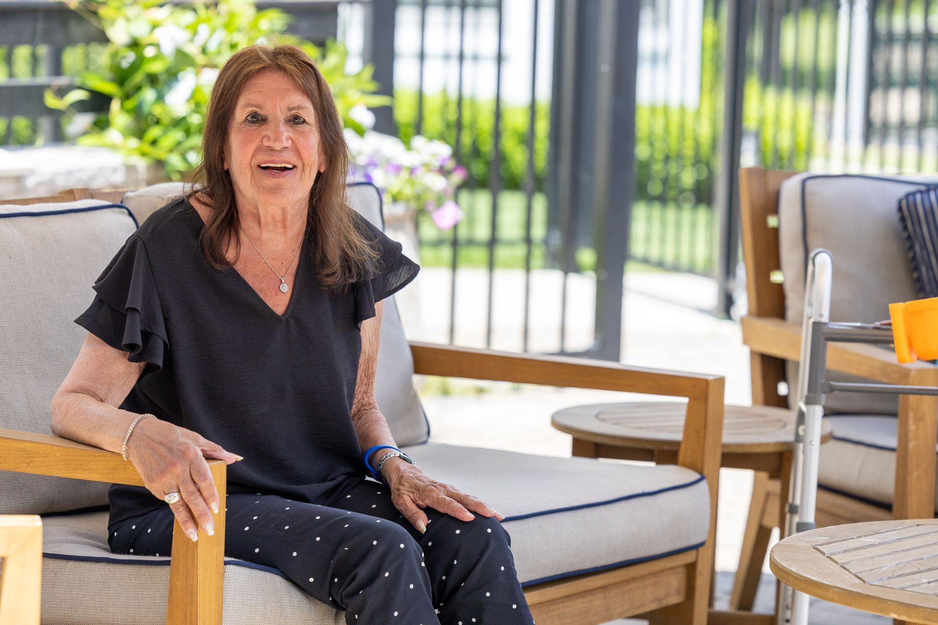 Woman seated outdoors on a patio, smiling beside a cushioned chair and table.