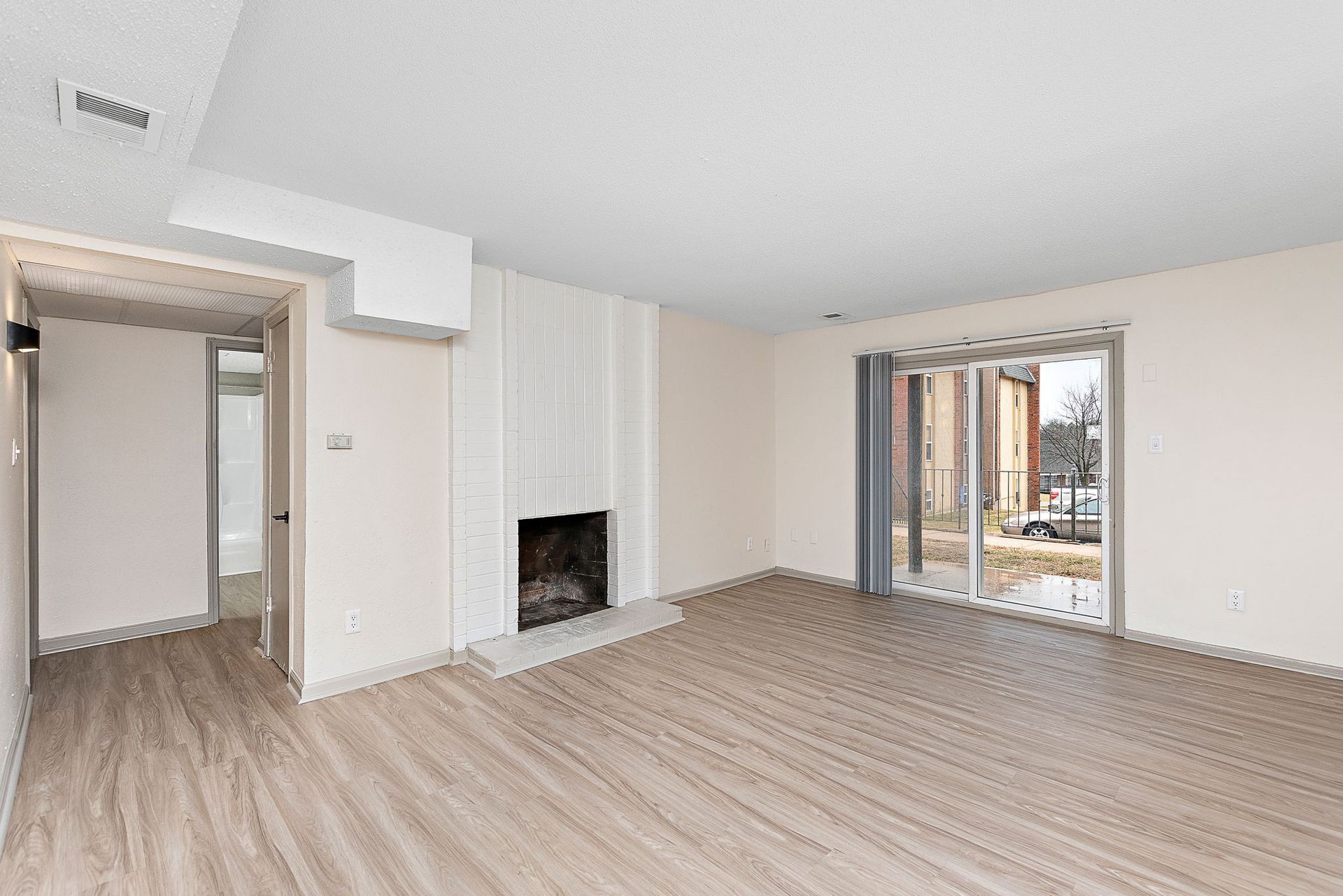 Empty modern living room with light wood floors, white walls, and a fireplace.