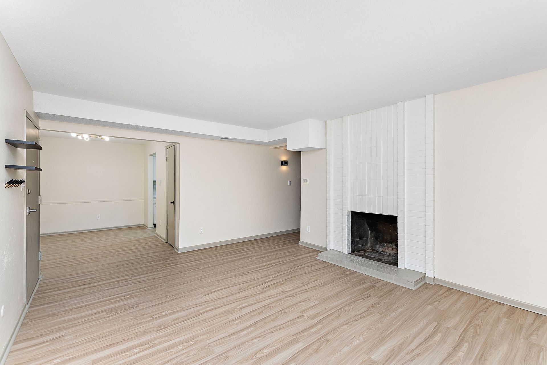Empty living room with white walls, beige carpet, and a white brick fireplace.