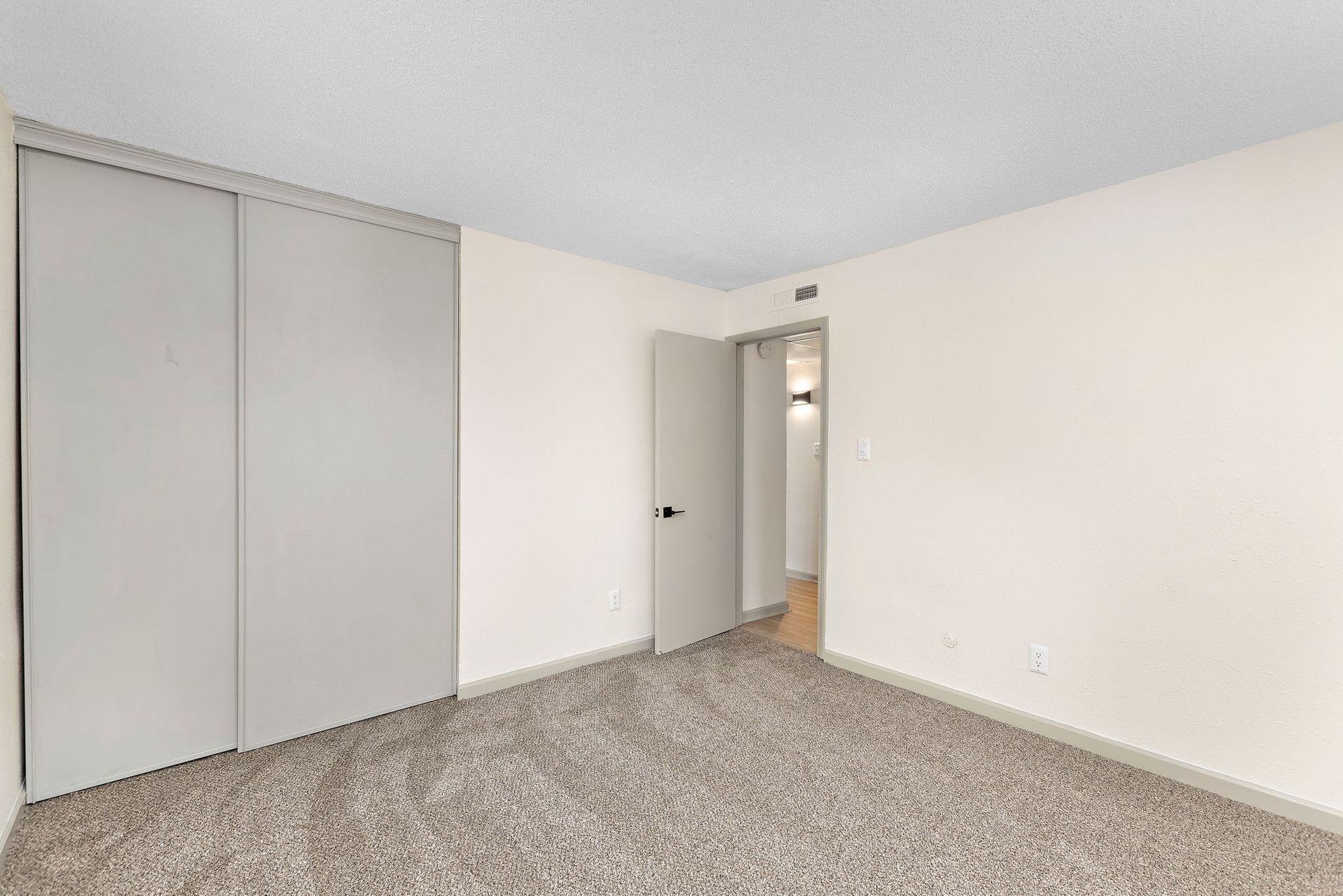 Empty carpeted bedroom with gray closet doors and an open doorway