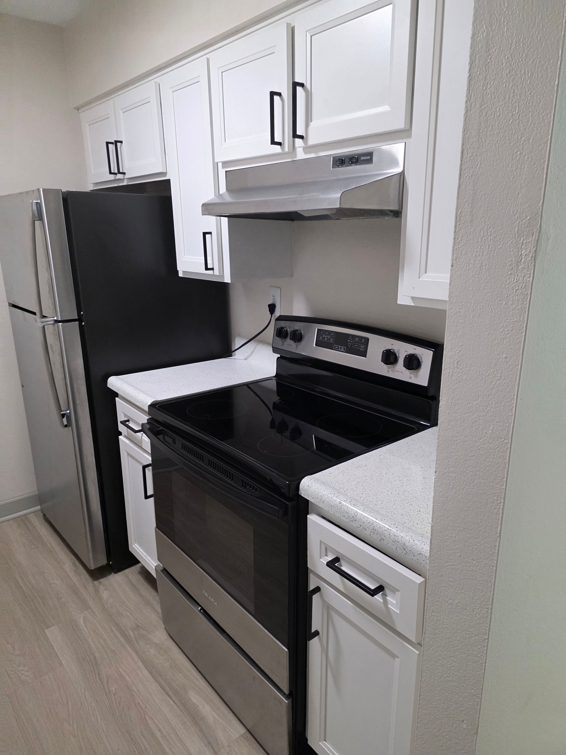 Small kitchen with stainless steel refrigerator and stove, white cabinets, and a light countertop.