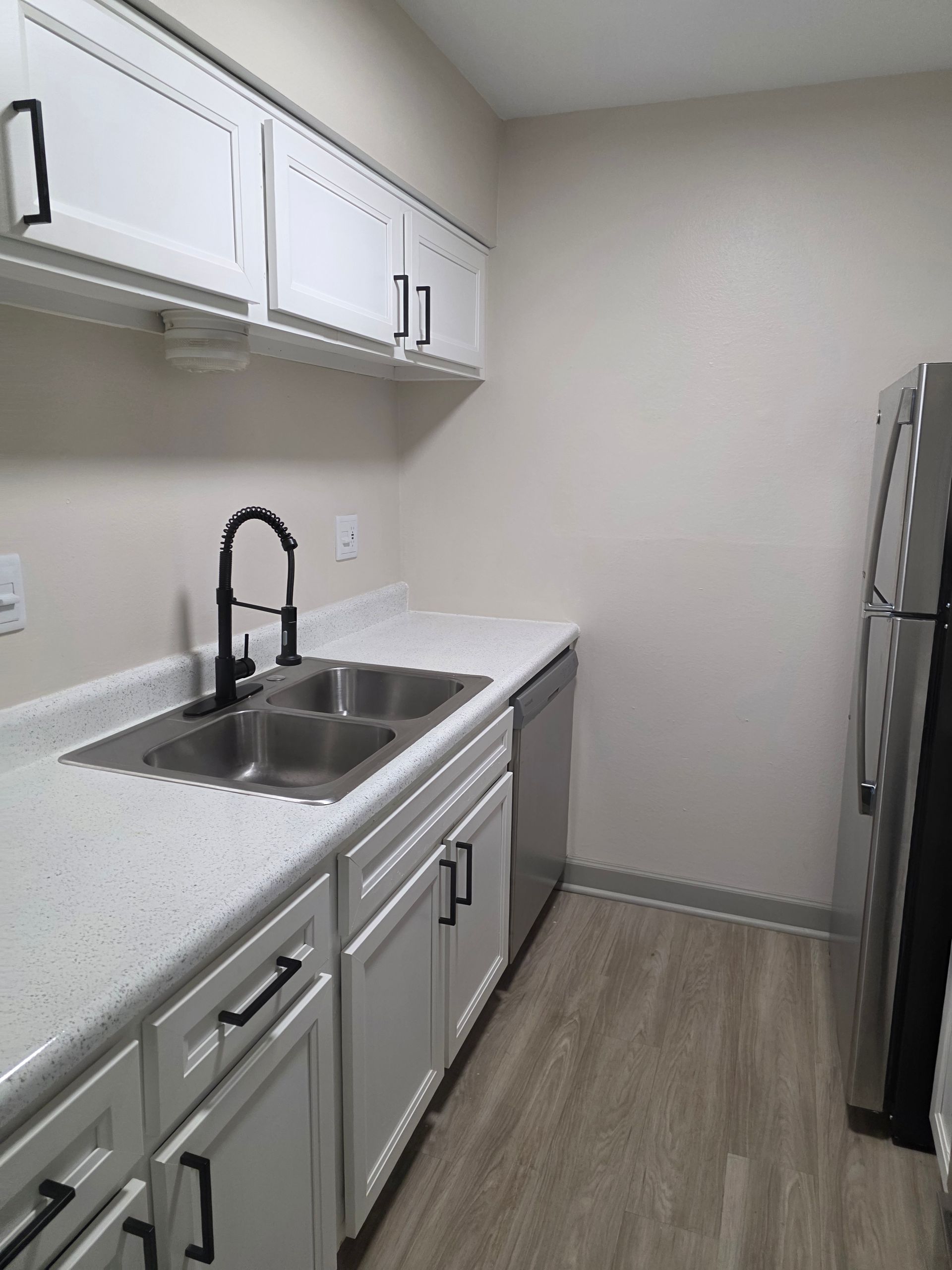 Bright white kitchen with black faucet, double sink, white cabinets, and light wood floor.