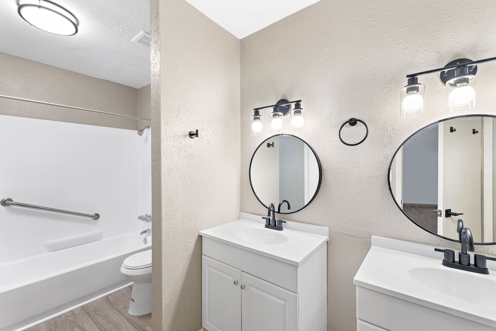 Bright bathroom with double vanity, round mirrors, wall lights, and a bathtub with shower curtain