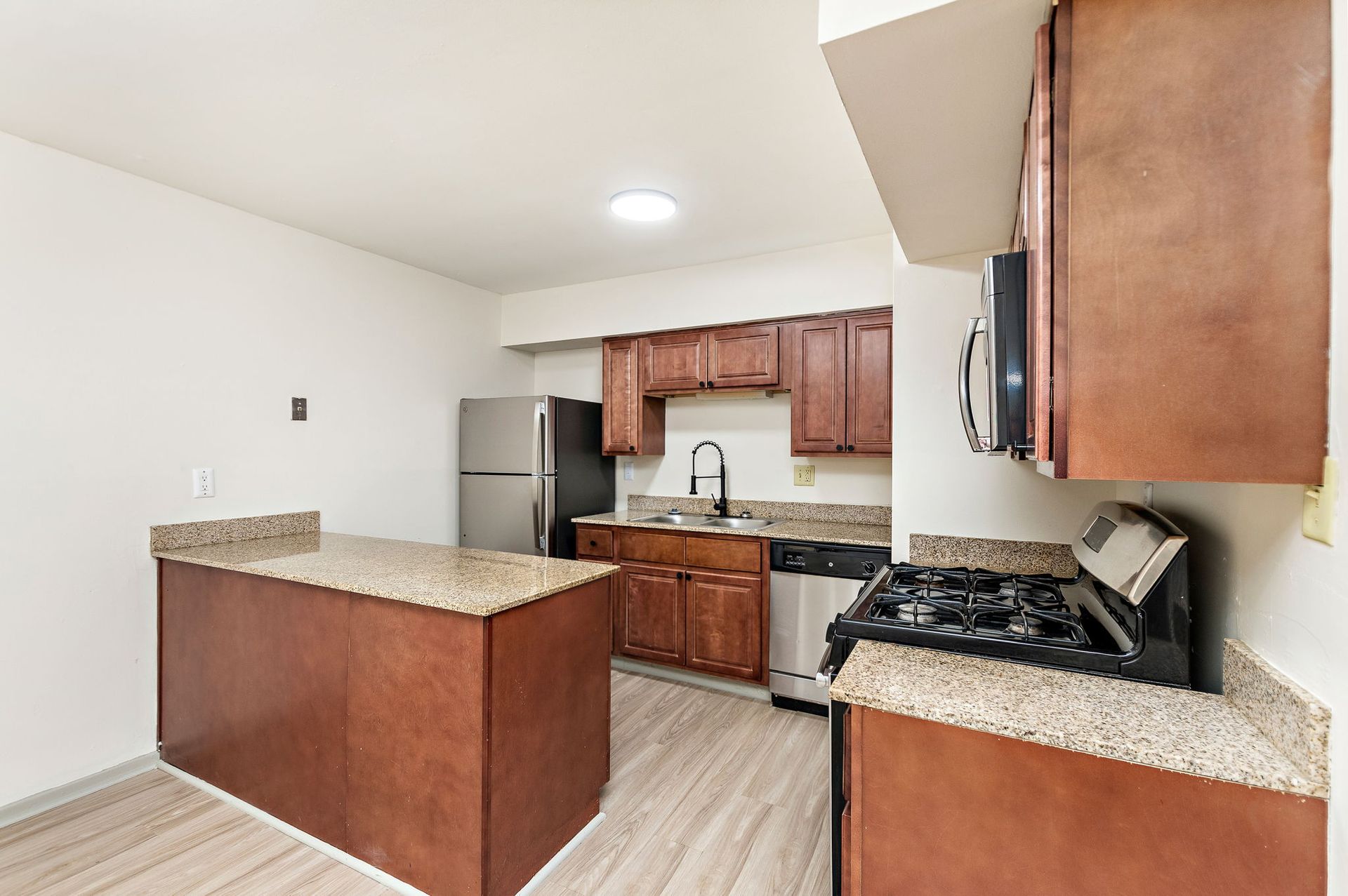 Compact kitchen with wood cabinets, granite counters, stainless fridge, and a peninsula island.