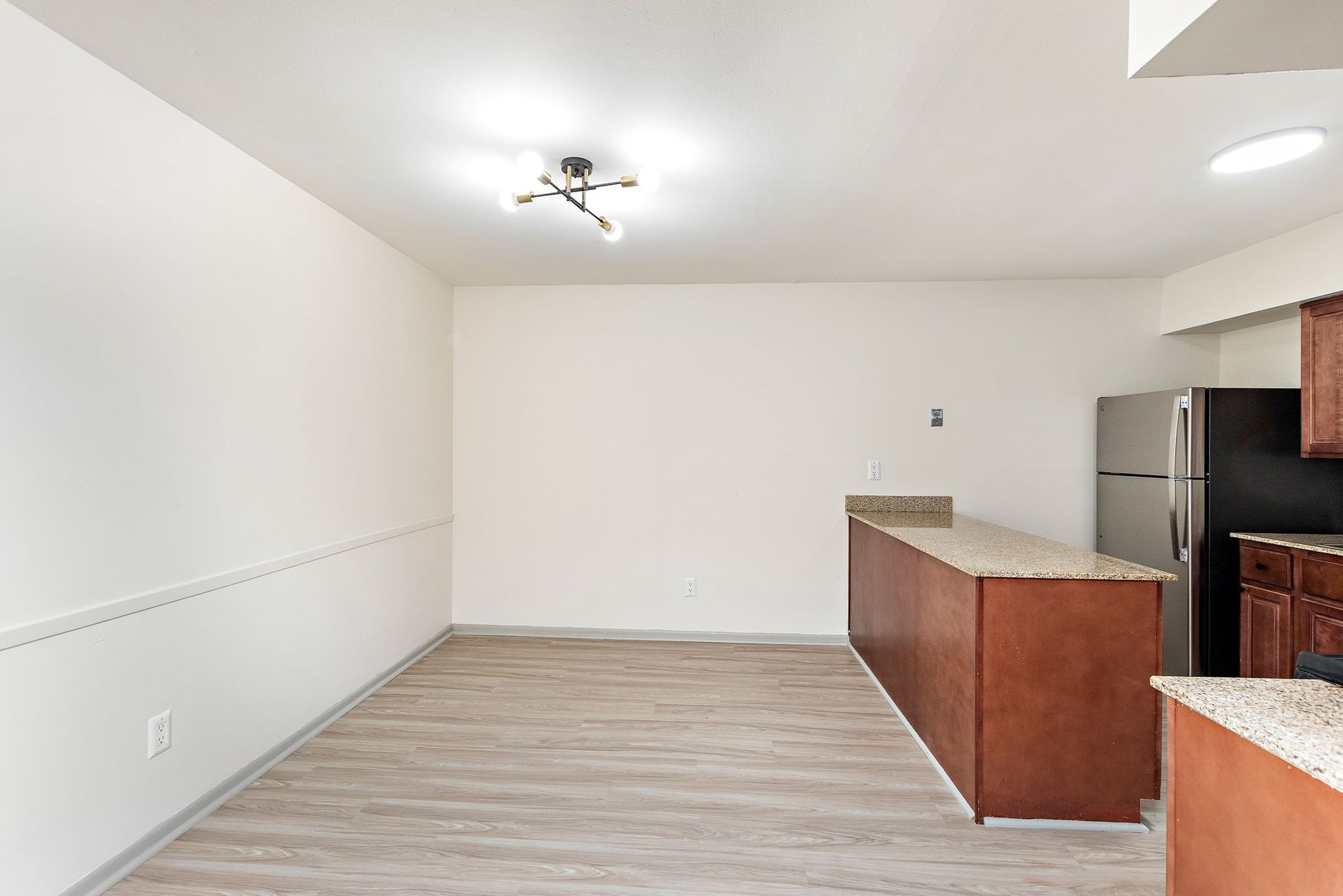 Empty open-plan kitchen and living area with light wood floors, white walls, and granite countertops.