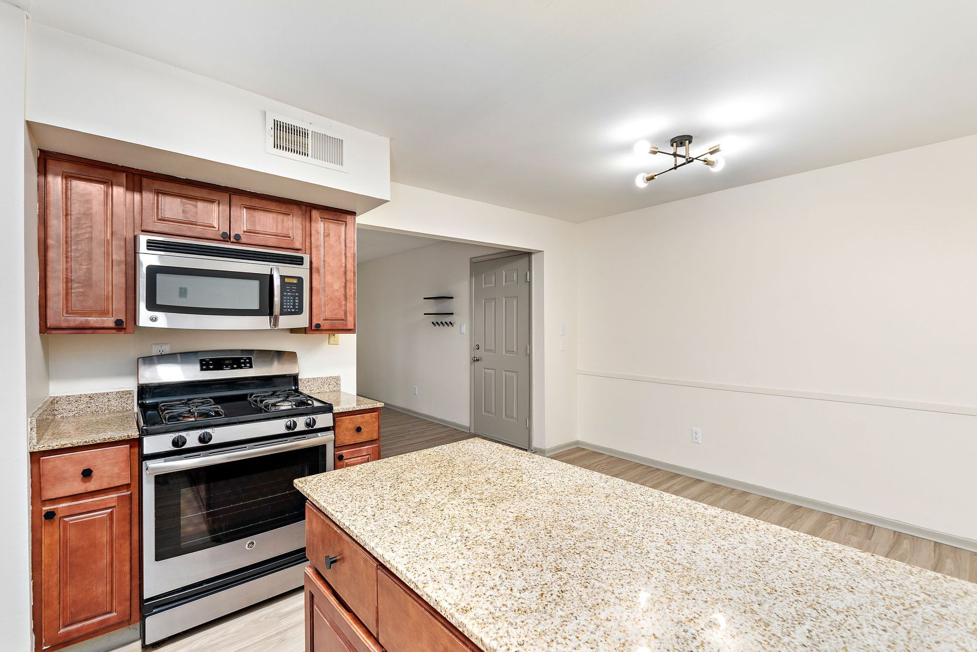 Small kitchen with granite island, stainless steel stove and microwave, wood cabinets, and white walls.