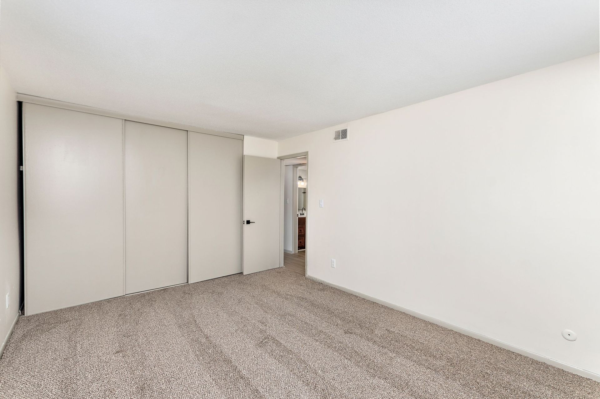 Empty beige bedroom with carpet, white walls, and sliding closet doors