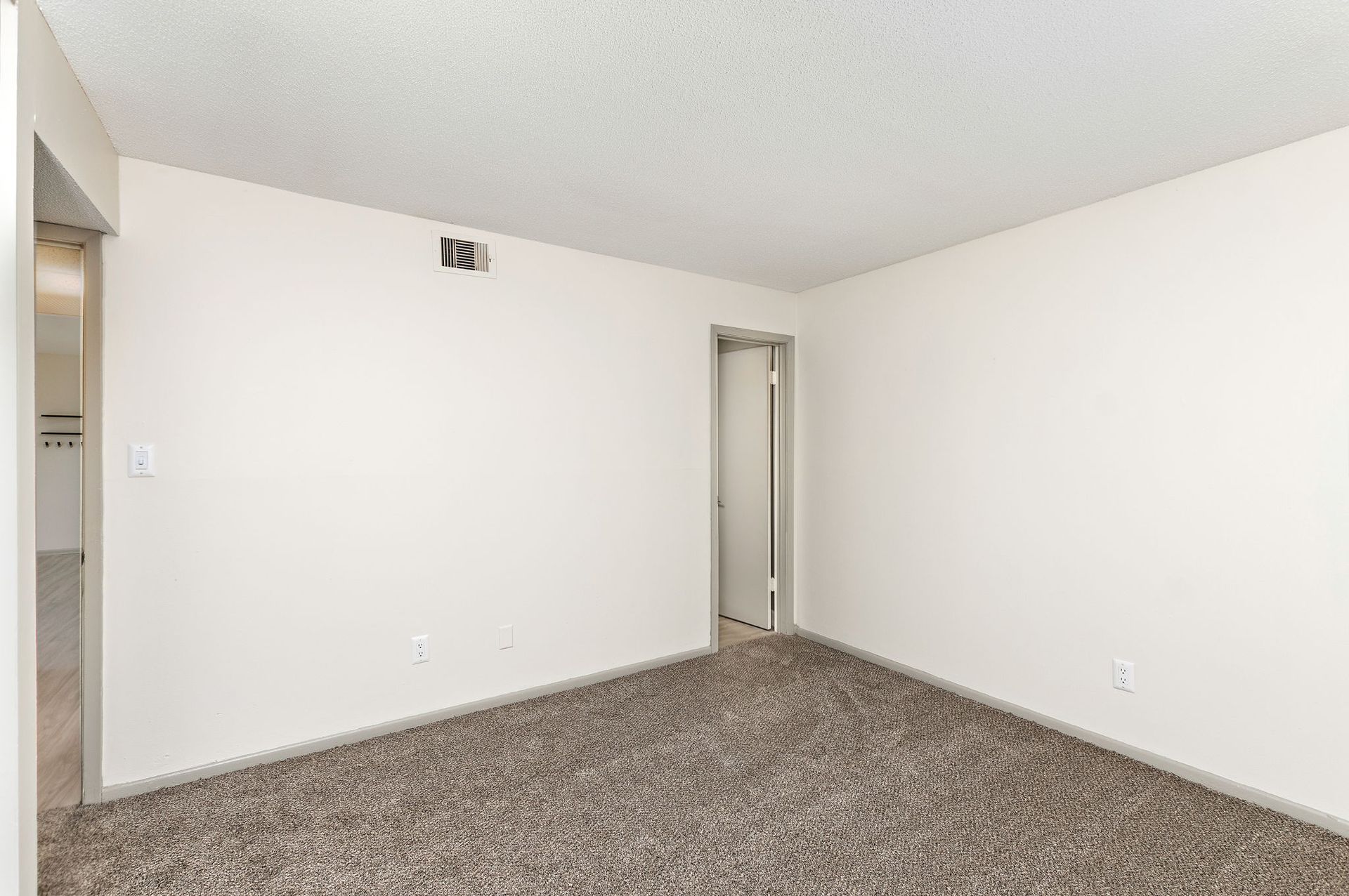 Empty beige bedroom with carpet and two doorways on white walls