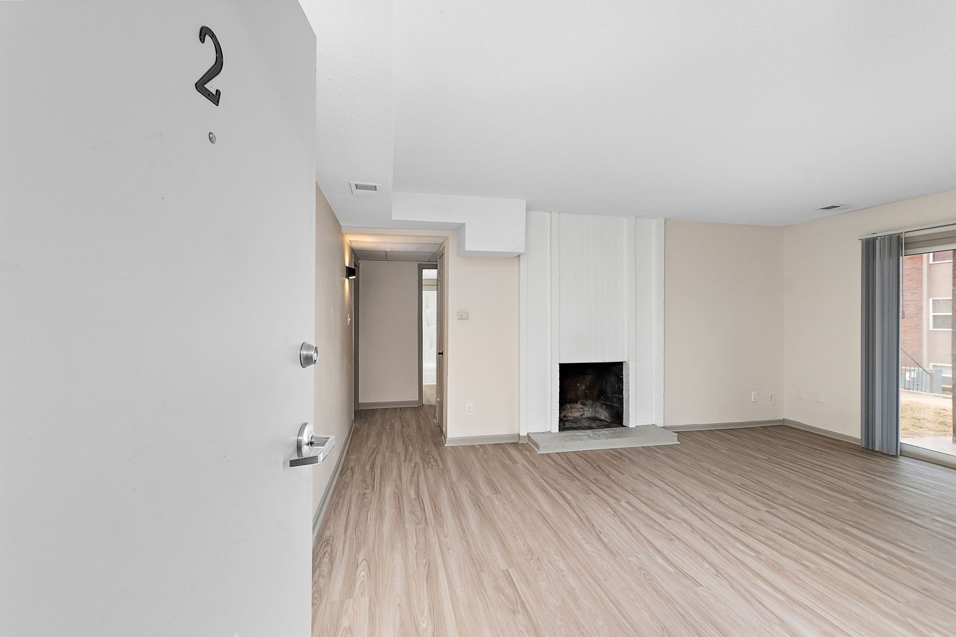 Empty modern living room with wood floors, fireplace, and open doorway to hallway