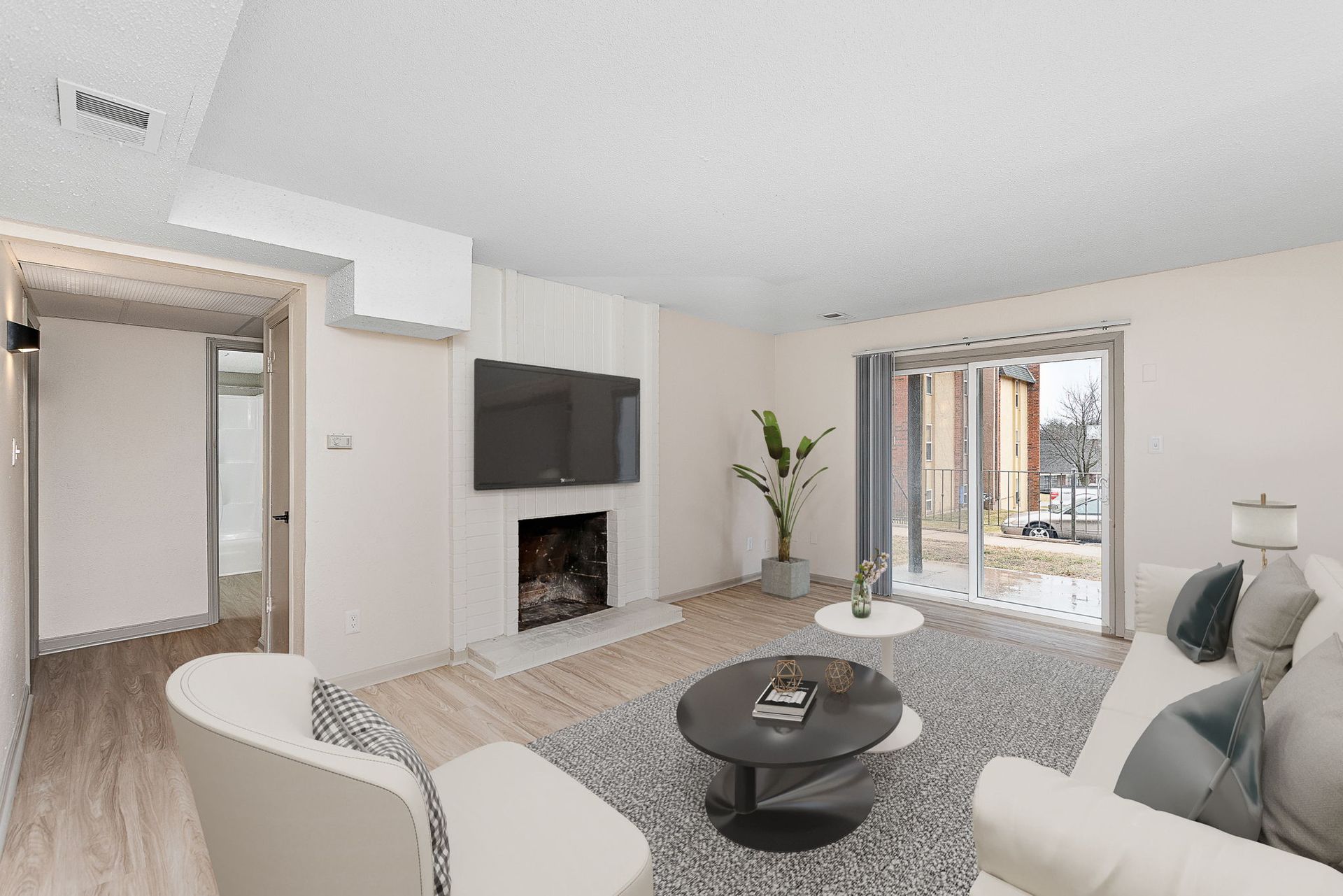 Bright living room with white seating, wall-mounted TV, fireplace, and sliding glass doors to a patio
