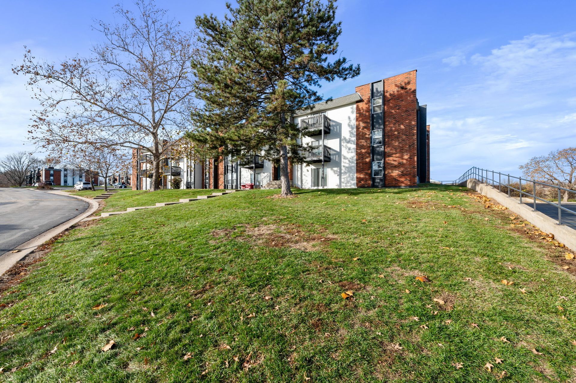 Modern brick-and-glass building on a grassy hill beside a curving road on a clear day