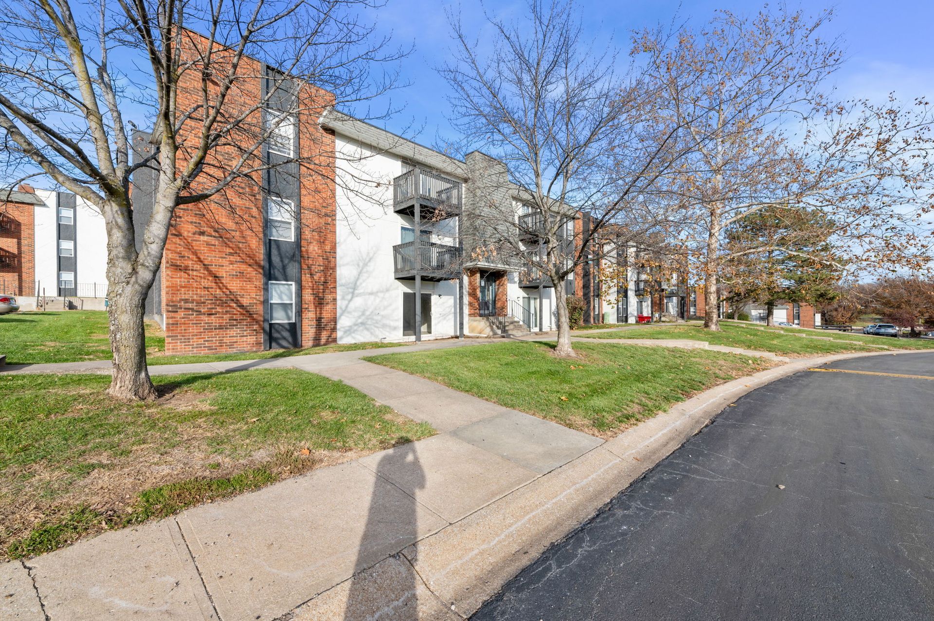 Apartment buildings beside a curved road with trees and sidewalks on a sunny day