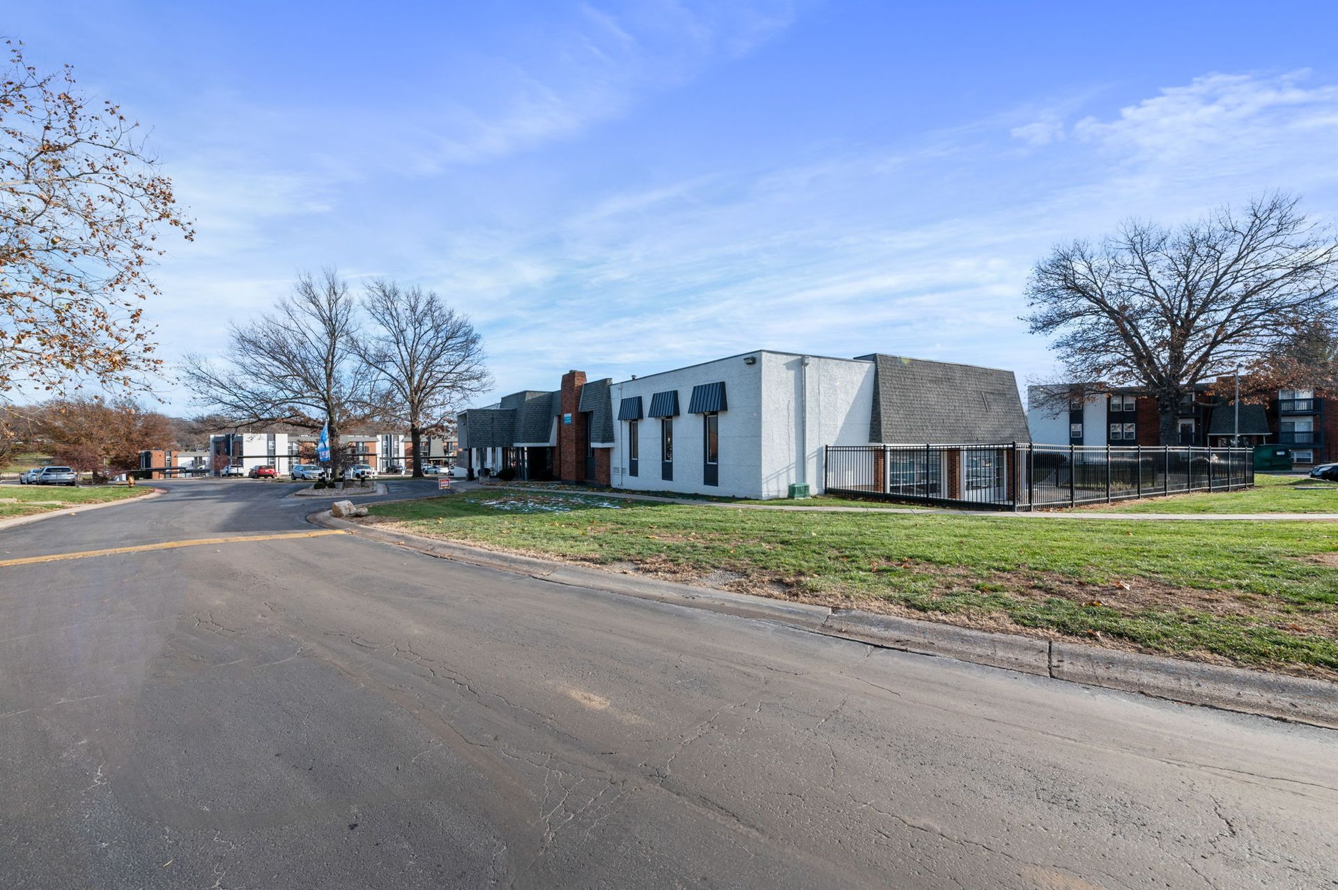 Modern low-rise building beside a road, with leafless trees and a grassy field under a blue sky