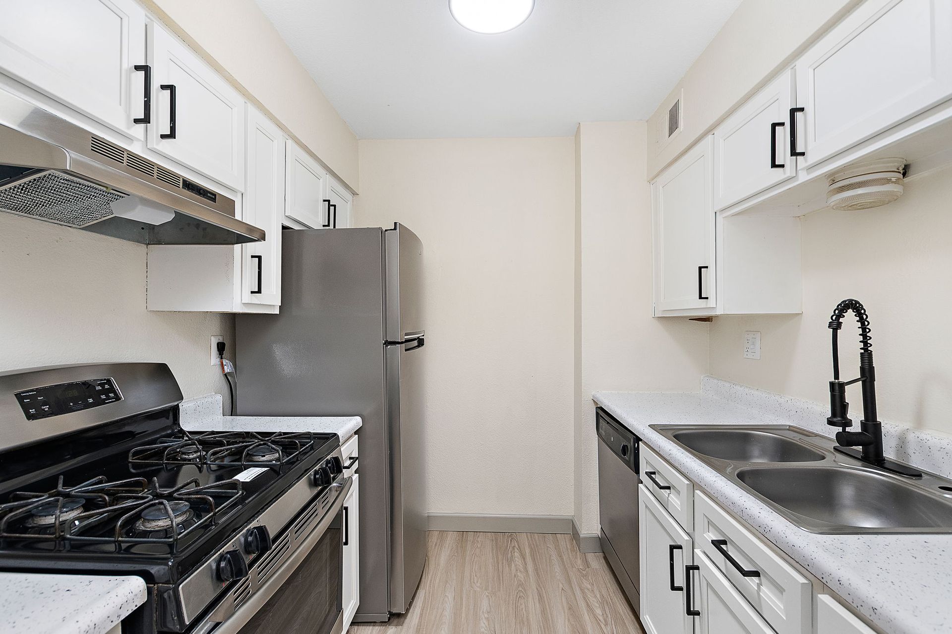 Bright galley kitchen with white cabinets, stainless-steel stove, and black faucet over a double sink.