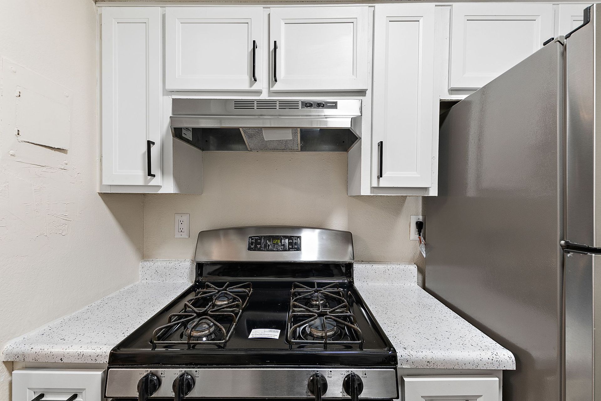 Small white kitchen with a stainless steel stove and refrigerator beneath white cabinets
