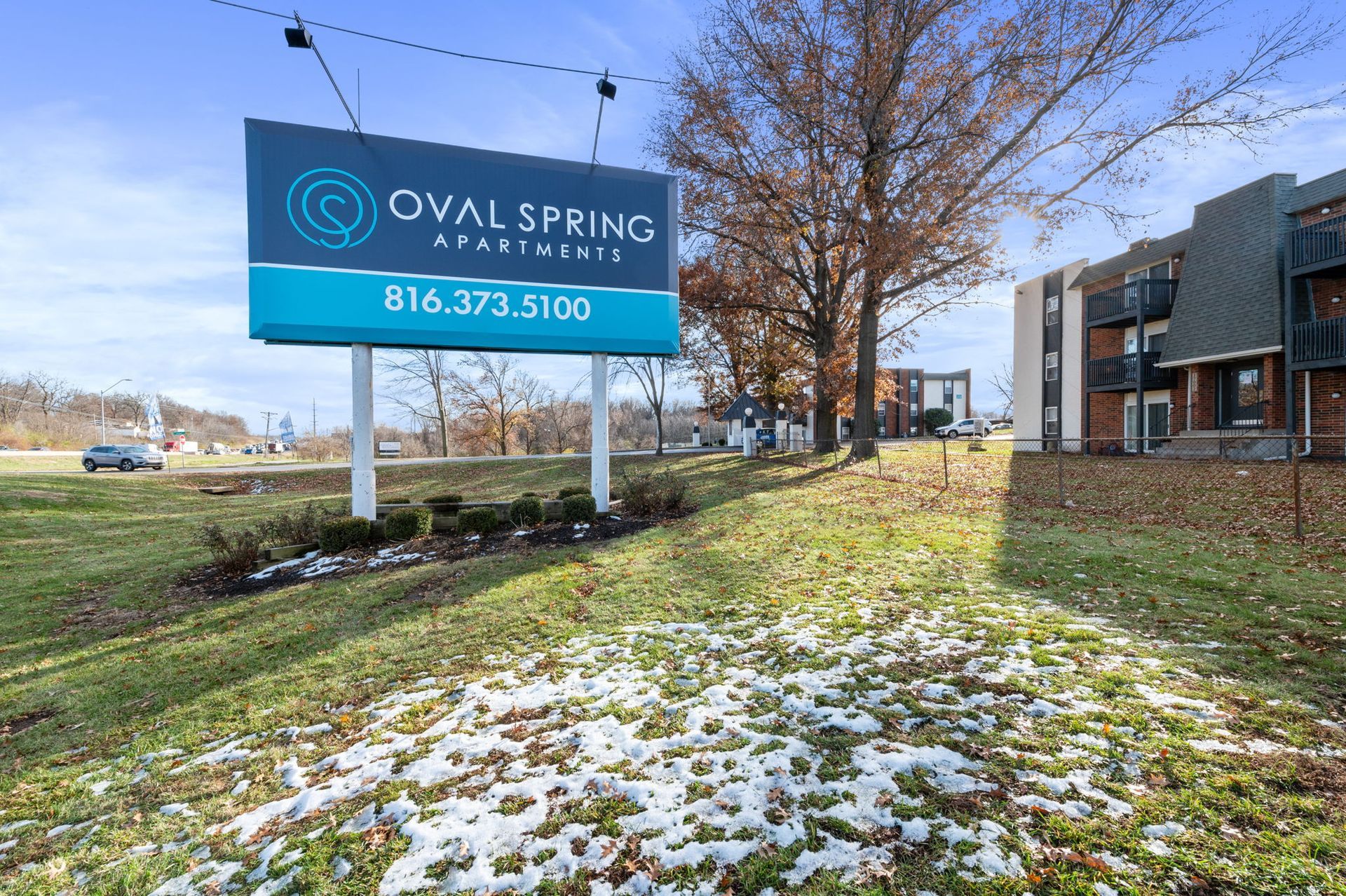 Oval Spring sign beside snowy grass and a brick building under a clear blue sky