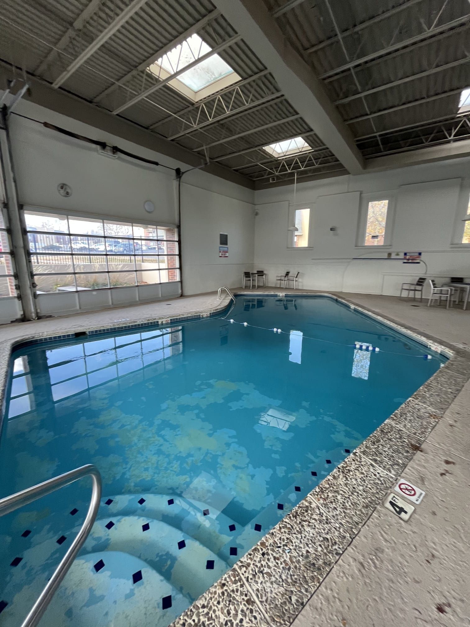 Indoor swimming pool with blue water, spa steps, and large garage-style windows in a bright room