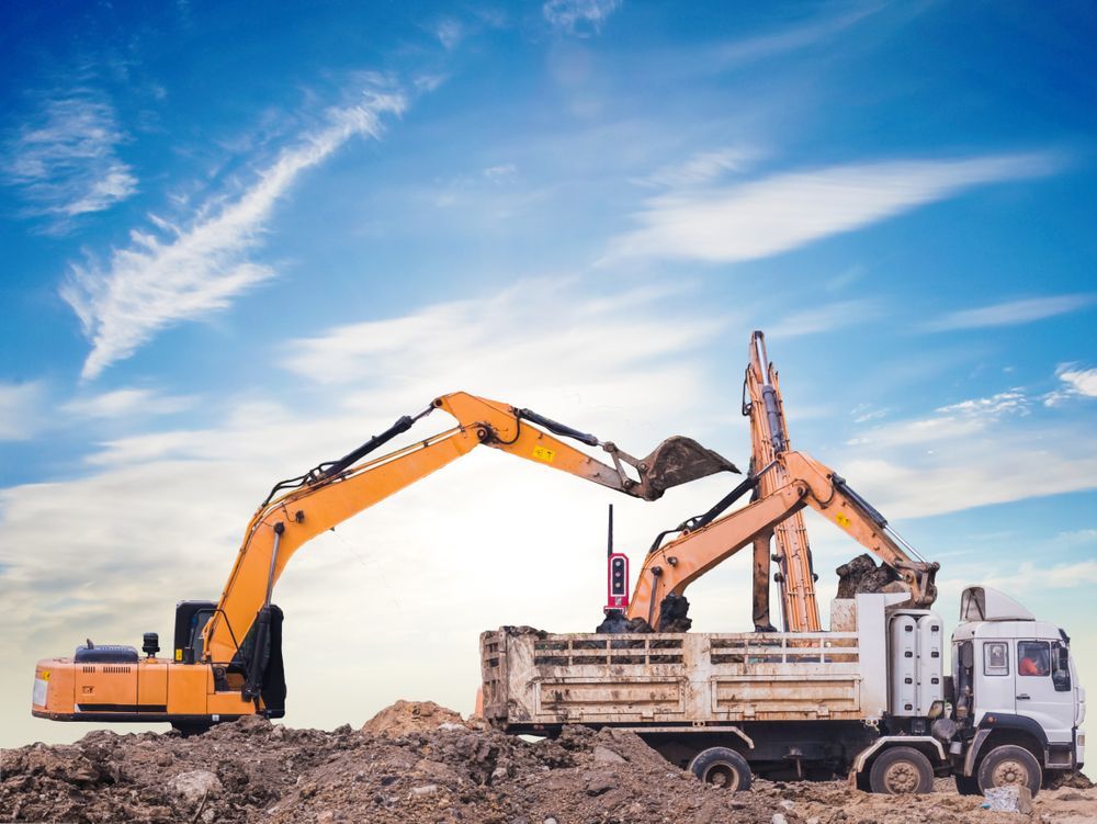 An Excavator Is Loading Dirt Into A Dump Truck At A Construction Site — Dubbo Hardcore Soils & Earthmoving In Dubbo, NSW