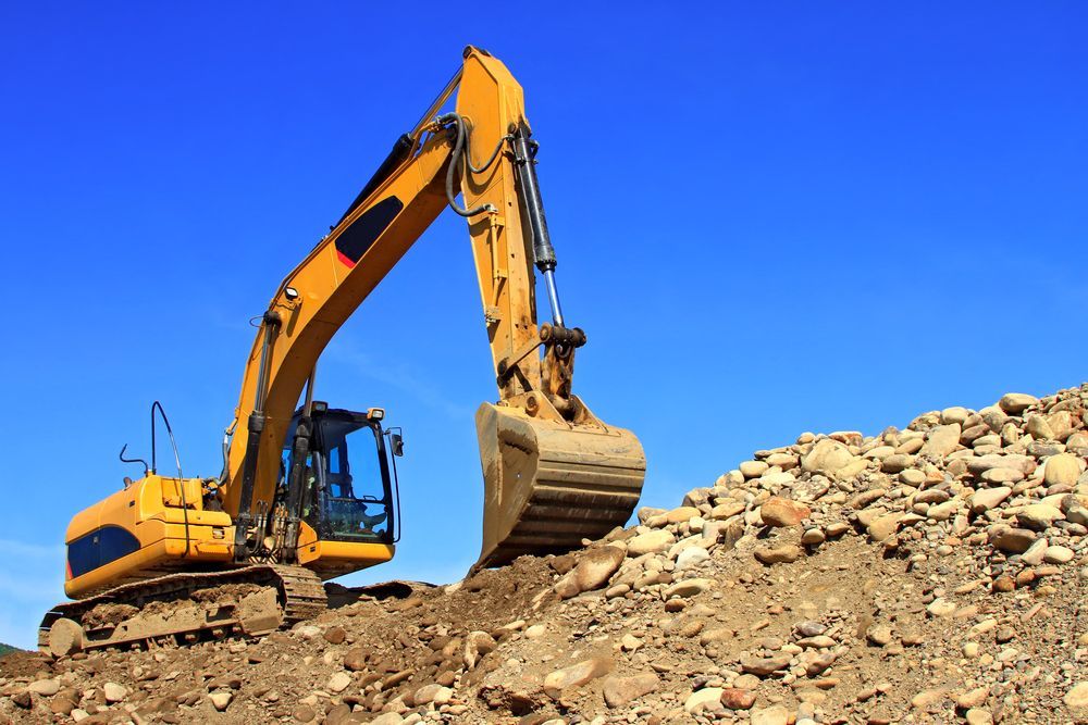 A Yellow Excavator Is Working On A Pile Of Rocks — Dubbo Hardcore Soils & Earthmoving In Dubbo, NSW