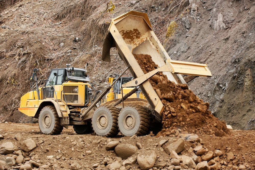 A Dump Truck Is Dumping Dirt Into A Pile Of Rocks — Dubbo Hardcore Soils & Earthmoving In Dubbo, NSW
